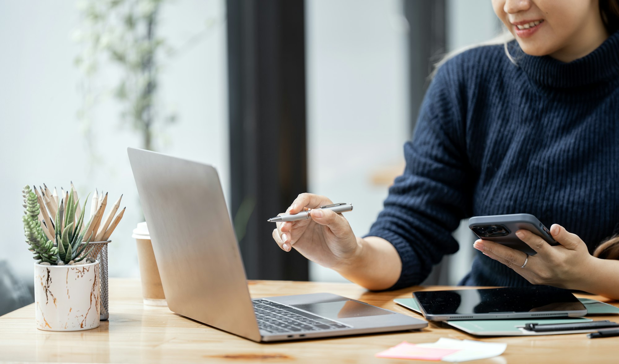 Young woman using mobile phone and laptop computer at office.